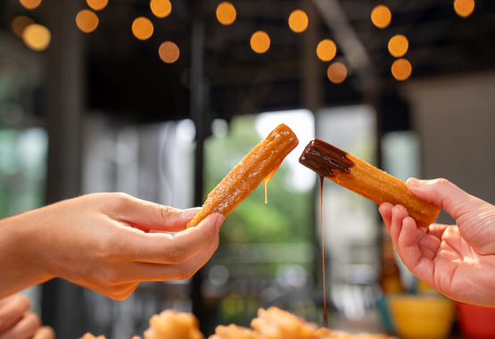 Hands holding churros. One is dipped in caramel and the other in chocolate sauce
